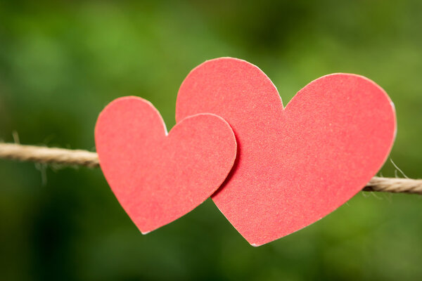 two red paper hearts hanging on the Natural background.