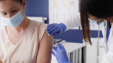 Maskeli bir doktor aşı yapar.