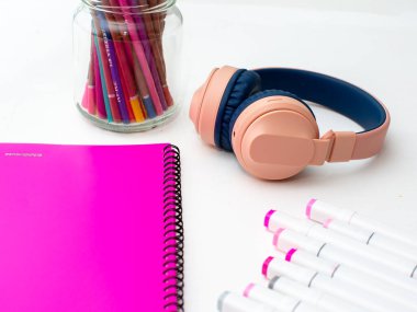 Masaüstü görüntüsü. Profesyonel çok renkli kalemler, pembe klasör, kulaklık.