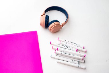 Masaüstü görüntüsü. Profesyonel çok renkli kalemler, pembe klasör, kulaklık.