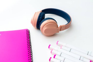 Masaüstü görüntüsü. Profesyonel çok renkli kalemler, pembe klasör, kulaklık.