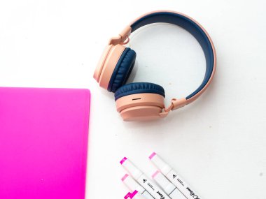 Masaüstü görüntüsü. Profesyonel çok renkli kalemler, pembe klasör, kulaklık.