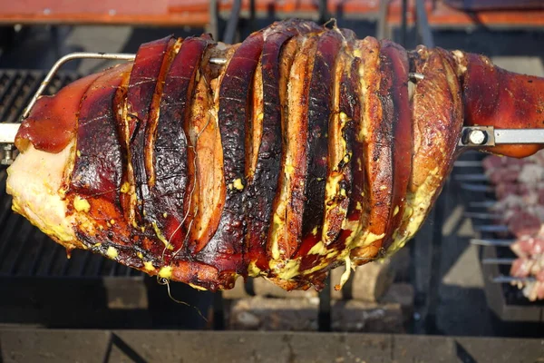 Un pezzo di maiale croccante su uno spiedo di rosticceria ad un evento barbecue. grande pezzo di carne su uno spiedo — Foto Stock