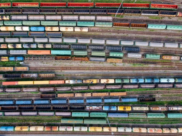 Top view on lots of various wagons: tanks, platforms, dump trucks staying on railways at depot. Cargo transportation of various goods by rail. Import and export logistics. Industrial aerial landscape.