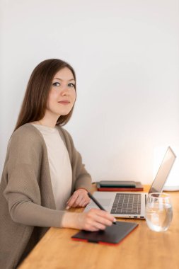 Laptop ve dijital tablette çalışan çekici beyaz bir kadın. Grafik tasarımcısı ev ofisinden çalışıyor. Boş beyaz ekran, boşluğu kopyala. Ahşap çalışma alanı. Serbest konsept.