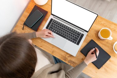 Tanımlanamayan esmer kız resim çiziyor ya da grafik tablet üzerinde fotoğraf rötuşluyor. Tahta not defterine, akıllı telefona, laptopa ve bir fincan çaya. Model için boş beyaz ekran. Üst manzara, düz uzanma.