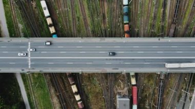Köprünün yukarısından hareket eden arabalarla çekilmiş hava görüntüleri. Köprünün altında birçok tren yolu var. Yük vagonları ve tankları olan trenler onların yanından geçiyor. Lojistik ithalat ve ihracat. Yük terminali.