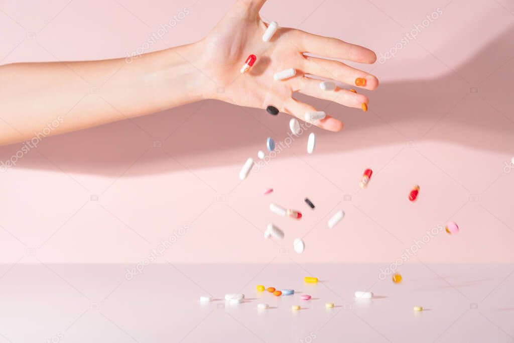 Various pills dropped from female hand on the table. Medicines for headache, colds, high fever, toothache and other diseases. Pink background. Drugs jump away from the table. Close up.