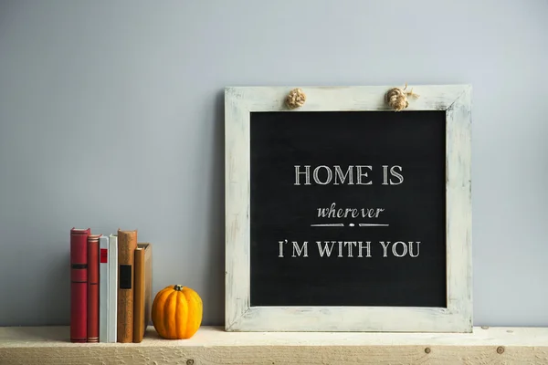 Chalkboard frame on the grey wall with books and pumpkin HOME IS — Stock Photo, Image