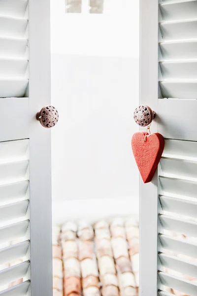 Corazón de madera roja colgando en la ventana de la terraza blanca —  Fotos de Stock