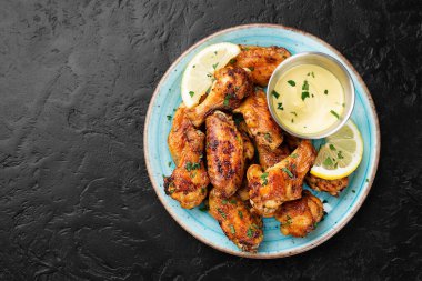 Farklı soslar ve limonla servis edilen fırında tavuk kanadı. Siyah arkaplan