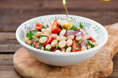 Beyaz fasulye salatası, kiraz domatesleri, kırmızı soğan ve ahşap arka planda maydanoz..