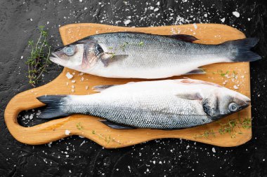Taze çiğ levrek ve siyah tahtada yemek pişirmek için malzemeler..