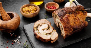 Kızarmış domuz eti, siyah taş masada otlar ve baharatlarla..