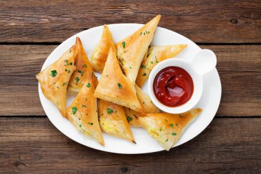Domates soslu ve otlu vejetaryen samsa (samosas). Patatesle doldurulmuş. ahşap arkaplanda