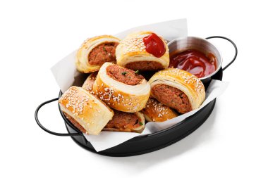 Beyaz arka planda domates sosuyla servis edilen lezzetli ev yapımı sosisli börekler.