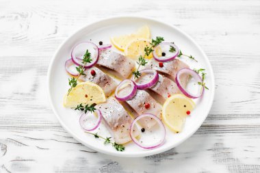 Baharatlı tuzlu ringa balığı, limon ve kırmızı soğan halkaları beyaz ahşap arka planda. Salamura edilmiş balık.. 