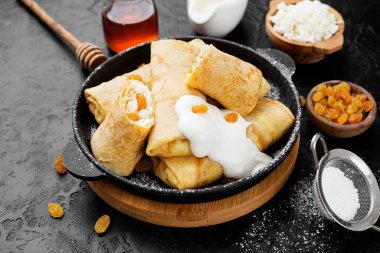 Süzme peynirle doldurulmuş ince krepler ya da krepler ve siyah arka planda kuru üzümler. 