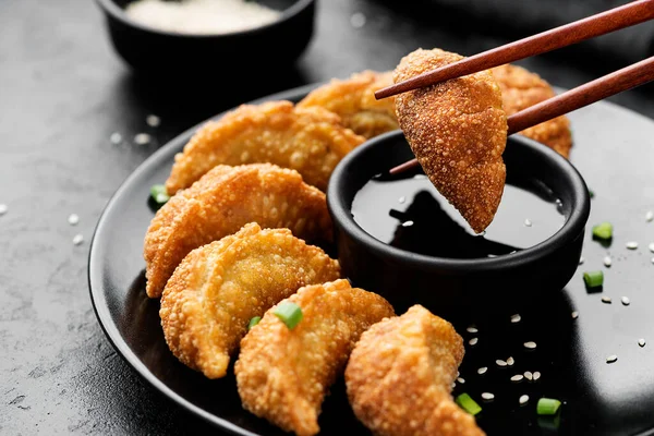 黒の質感を背景に 箸と醤油ゴマソースをかけた黒陶板の上にアジアの餃子フライ餃子ポッステッカー — ストック写真