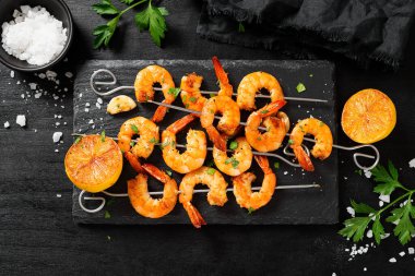 Grilled shrimp skewers. Shrimps with herbs, garlic and lemon on black background.	