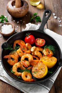 Prawns Shrimps roasted on frying pan with lemon and garlic on wooden background.	