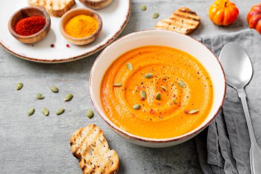 Pumpkin and carrot soup with spices on on grey stone background.	