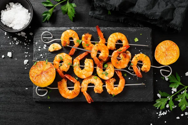 Grilled shrimp skewers. Shrimps with herbs, garlic and lemon on black background.