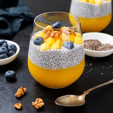 Vegan chia pudding with mango puree, blueberries and granola in a glass .	