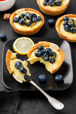 Blueberry tartlet, pie, tart with lemon custard. Black stone background.	