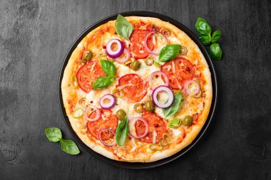 Eritilmiş mozarella peynirli İtalyan pizzası yeşil zeytin ve taze sebze ve fesleğen yapraklarıyla süslenmiş domates..