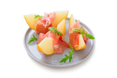 Jambonlu dilimlenmiş kavun (prosciutto) ve roka yaprakları. Beyaz arka planda izole edilmiş.