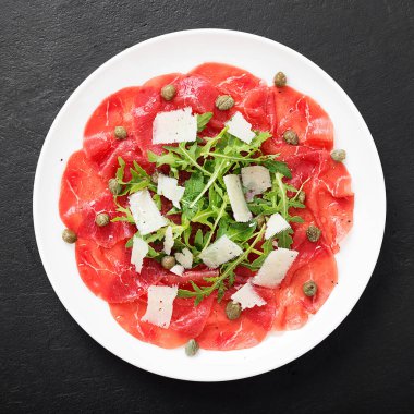 Carpaccio bifteği, parmesanlı soğuk aperatif kapari ve beyaz tabakta roka. Üst görünüm.
