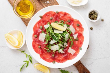 Carpaccio bifteği, parmesanlı soğuk aperatif, kapari ve roka beyaz tabakta..