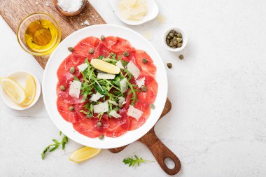 Carpaccio bifteği, parmesanlı soğuk aperatif, kapari ve roka beyaz tabakta..
