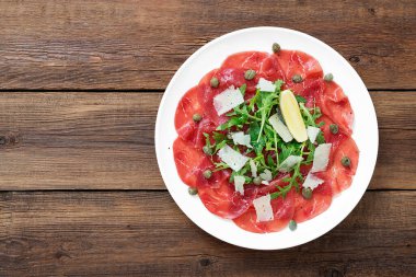 Carpaccio bifteği, parmesanlı soğuk aperatif, kapari ve roka beyaz tabakta..