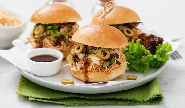 Pulled chicken sandwiches with barbeque sauce and lettuce on light blue or gray background.