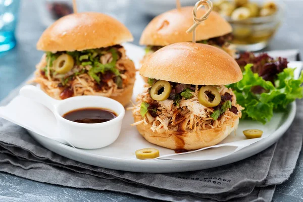 Pulled chicken sandwiches with barbeque sauce and lettuce on light blue or gray background.