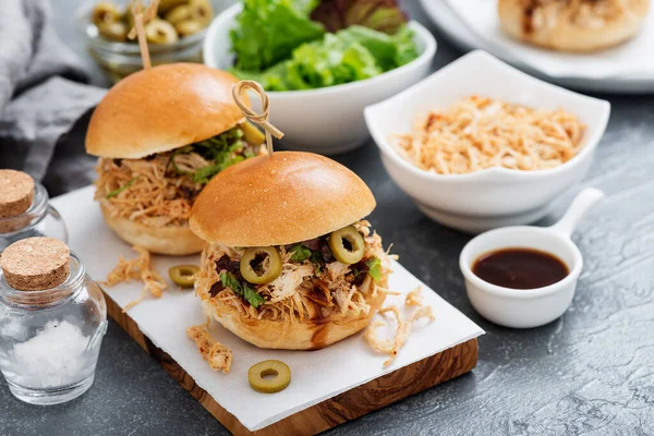Pulled chicken sandwiches with barbeque sauce and lettuce on light blue or gray background.
