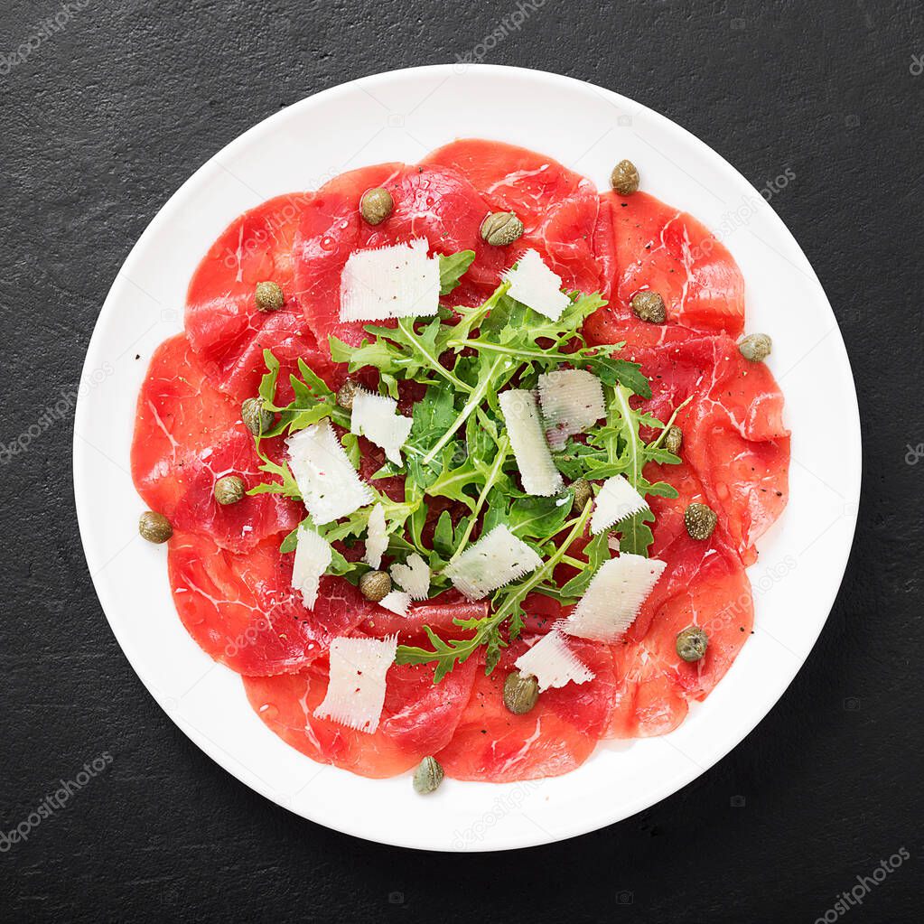 Beef Carpaccio cold appetizer with parmesan, capers and arugula on white plate. Top view.
