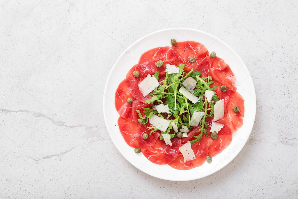 Beef Carpaccio cold appetizer with parmesan, capers and arugula on white plate.Top view.