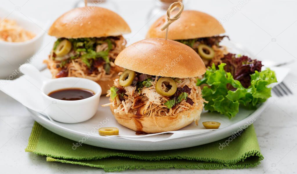Pulled chicken sandwiches with barbeque sauce and lettuce on light blue or gray background.