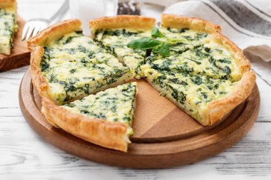 Beyaz ahşap arka planda beyaz peynirli vejetaryen ıspanaklı turta ya da tart..