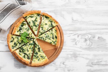 Beyaz ahşap arka planda beyaz peynirli vejetaryen ıspanaklı turta ya da tart..