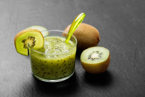 Blended kiwi smoothie with fresh fruits on black stone background.