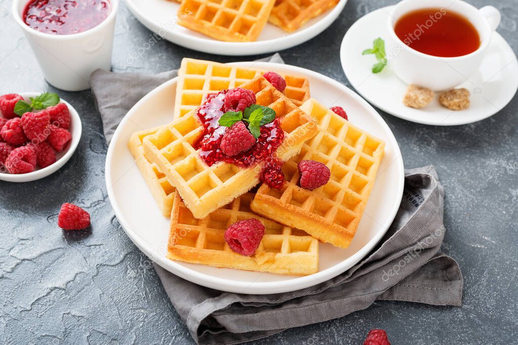 Traditional belgian waffles with fresh raspberry and jam on gray background.