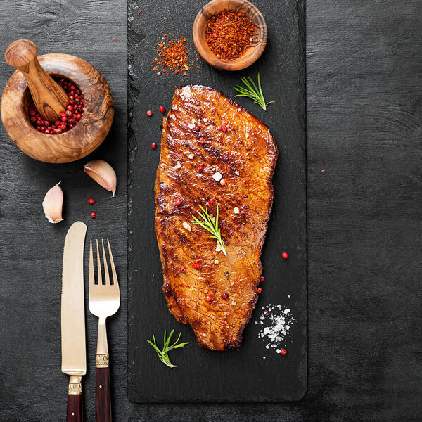 Sliced grilled beef steak with rosemary, salt and pepper on black stone plate. Top view