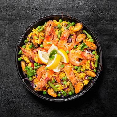 Geleneksel İspanyol deniz ürünleri paella 'sı, siyah ahşap bir masada, üst tarafta..