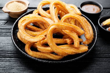 Siyah ahşap arka planda şeker ve çikolata soslu Churros..