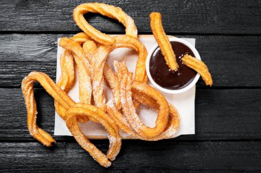Siyah ahşap arka planda şeker ve çikolata soslu Churros..