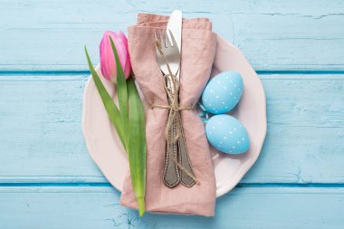 Paskalya arkaplanı pembe lale ve mavi ahşap masa üzerinde renkli yumurtalar..